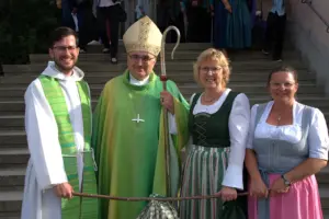 Zwei Männer in krichlichen Gewändern und zwei Frauen im Dirndl stehen vor einer Treppe
