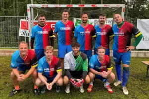 Eine Fußballmannschaft mit zehn Spielern posiert in blau-roten Trikots vor einem Tor. Auf den Trikots ist der Schriftzug „Polizei Bruck-Mürzzuschlag“ zu sehen.