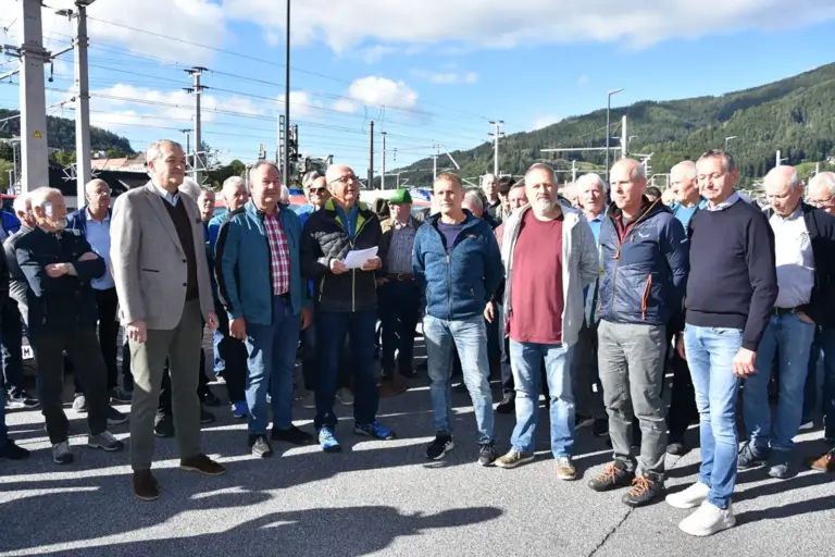 Mürzzuschlag: Ausflug der Feuerwehrsenioren Eine Gruppe von älteren Personen steht auf einem Gelände mit Bahnoberleitungen im HIntergrund