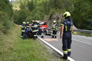 Feuerwehrmänner halten ein blaues Motorrad am Rand einer Landstraße, daneben steht ein Einsatzfahrzeug mit Anhänger
