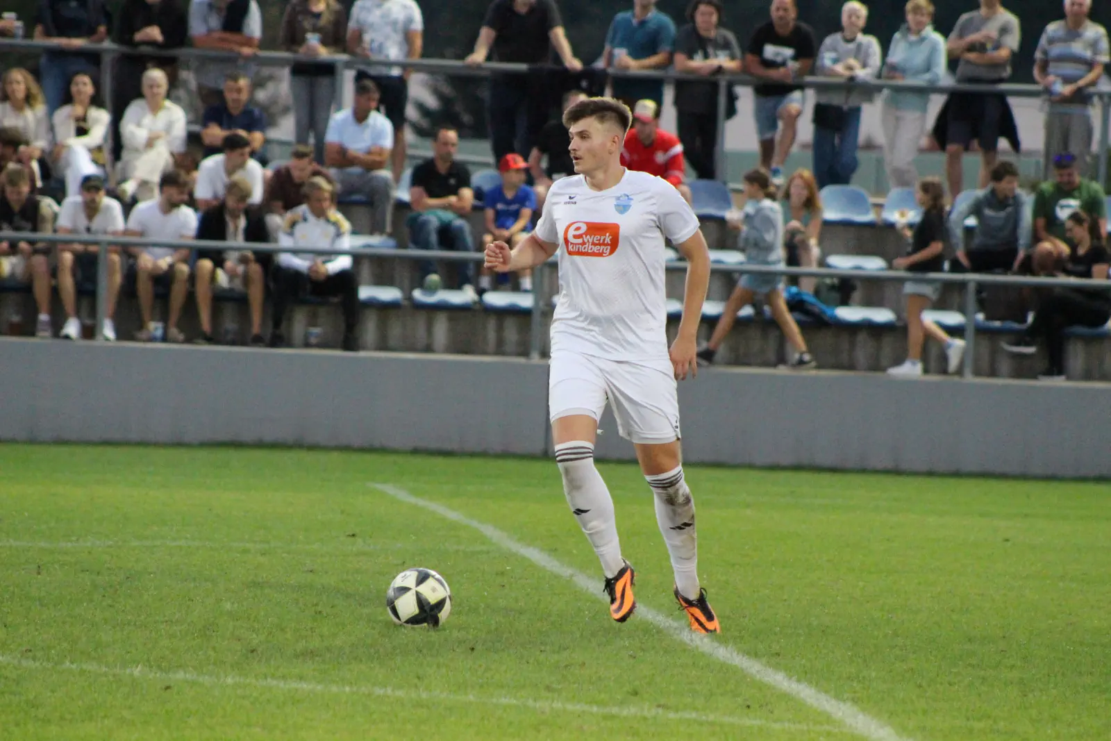 Ein Fußballer mit einem Ball, dahinter Zuseher.