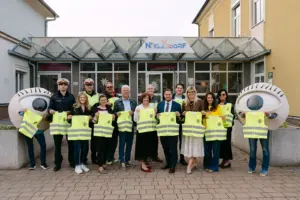 Eine Gruppe von Personen steht mit gelben Warnwesten vor einem Gebäude