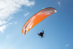 Ein schwebender Paragleiter von unten, der Pilot trägt einen Rotor auf dem Rücken.