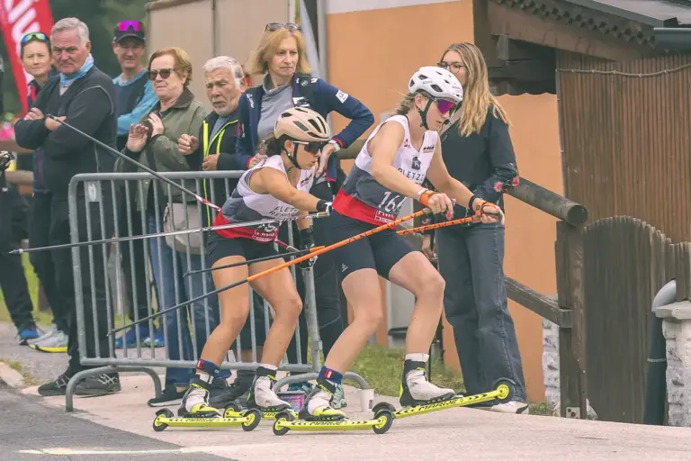 Schiroller-Elite zu Gast in Spital am Semmering Zwei Sportlerinnen mit Helmen und Skistöcken starten auf Skirollern zu einem Rennen. Hinter ihnen verfolgen mehrere Zuschauer das Geschehen.