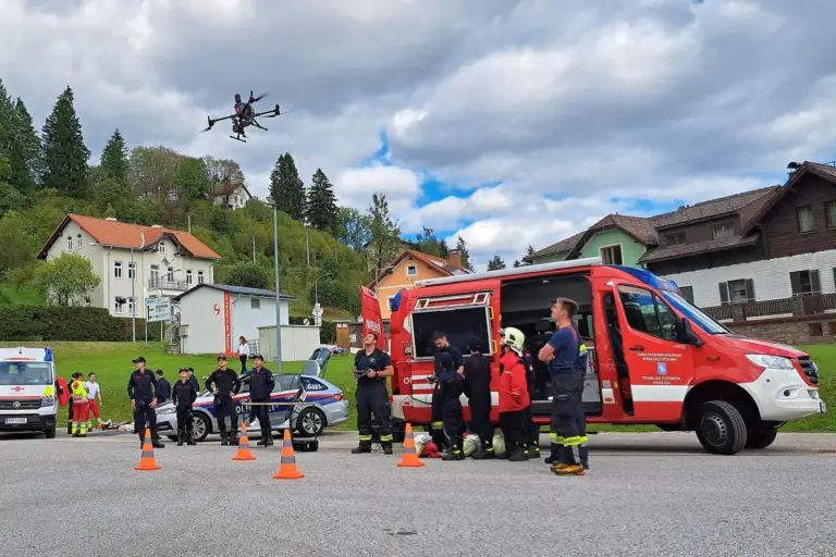 Mehrere Personen stehen vor einem Feuerwehrauto und beobachten eine Drohne
