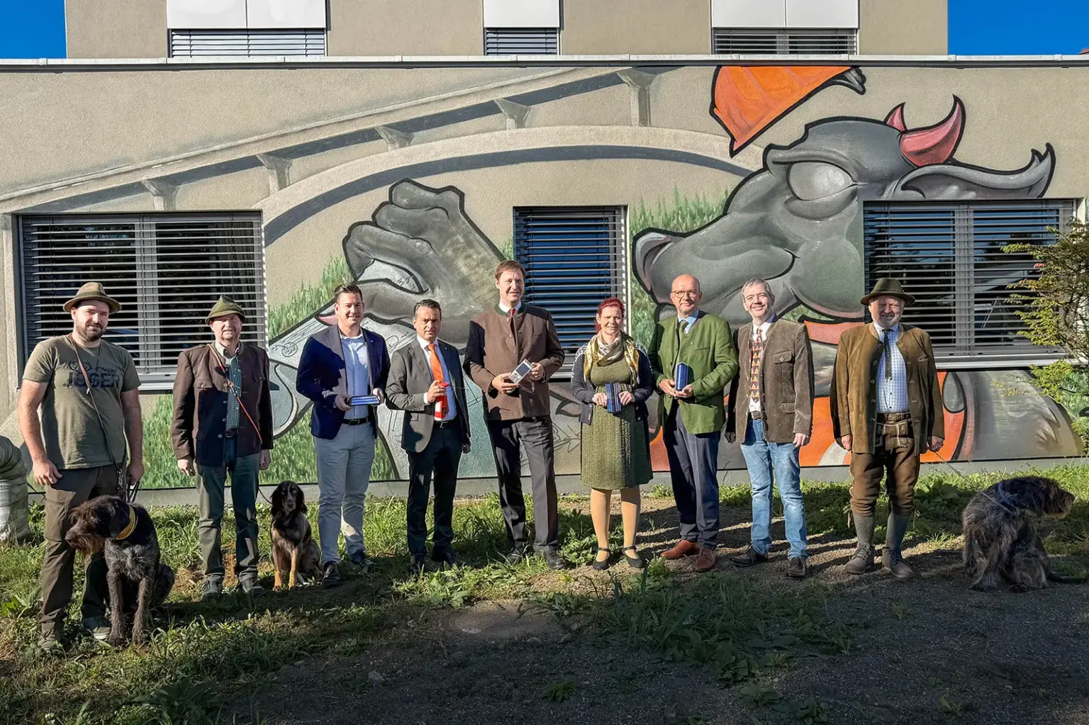 EIne Gruppe von Personen mit Hunden steht vor einer bemalten Wand