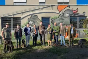 EIne Gruppe von Personen mit Hunden steht vor einer bemalten Wand
