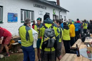 Viele Personen in Wanderkleidung stehen vor einer Berghütte