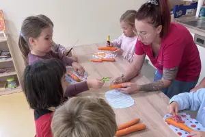 Mehrere Kinder sitzen um einen Tisch und verarbeiten gemeinsam mit einer Erwachsenen verschiedene Lebensmittel