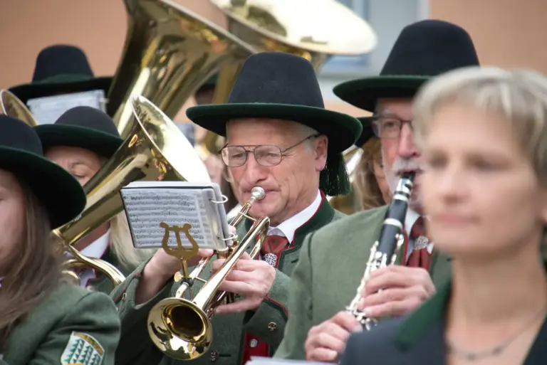 Ein Mann in Trachtenkleidung spielt Trompete, rings um ihn weitere Musikerinnen und Musiker