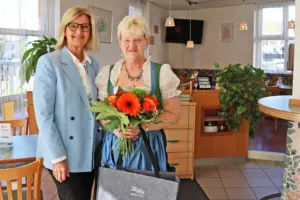 Zwei Frauen stehen mit einem Blumenstrauß in einer Gaststube