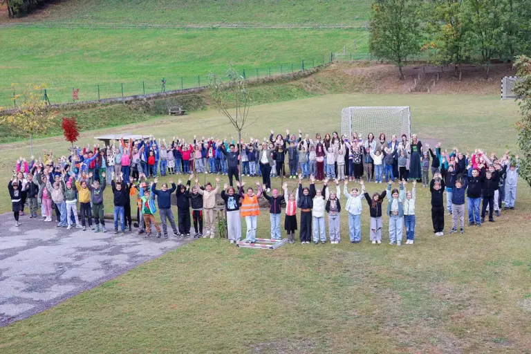 Volksschule Oberaich feierte Geburtstag Eine große Gruppe von Kindern steht rund um einen kleinen Baum auf einer Wiese