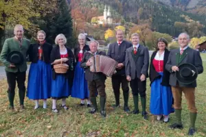 Mehrere Personen in Tracht stehen auf einer Wiese mit einer Kirche im Hintergrund