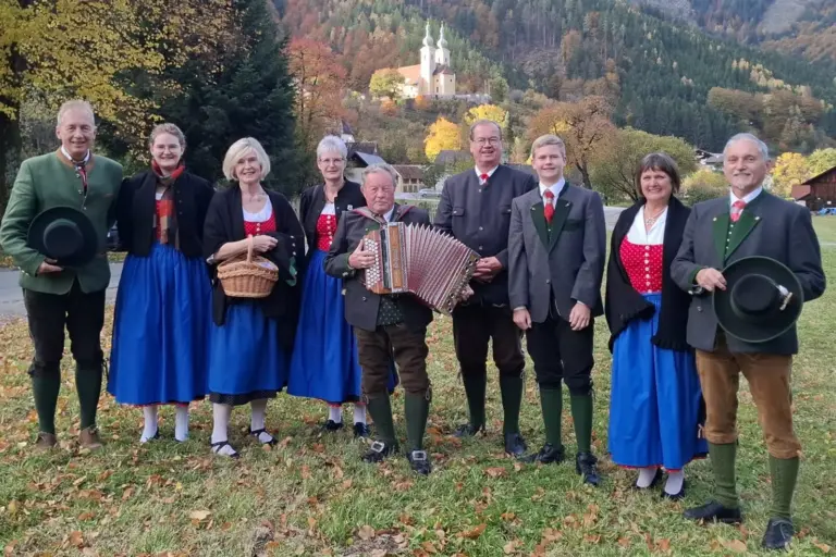 Maderecker aus Bruck zu Gast in Radmer Mehrere Personen in Tracht stehen auf einer Wiese mit einer Kirche im Hintergrund