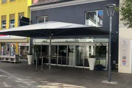 Brucker Café Schloffer wieder geschlossen Eine graue Fassade mit Auslage, davor ein großer grauer Sonnenschirm