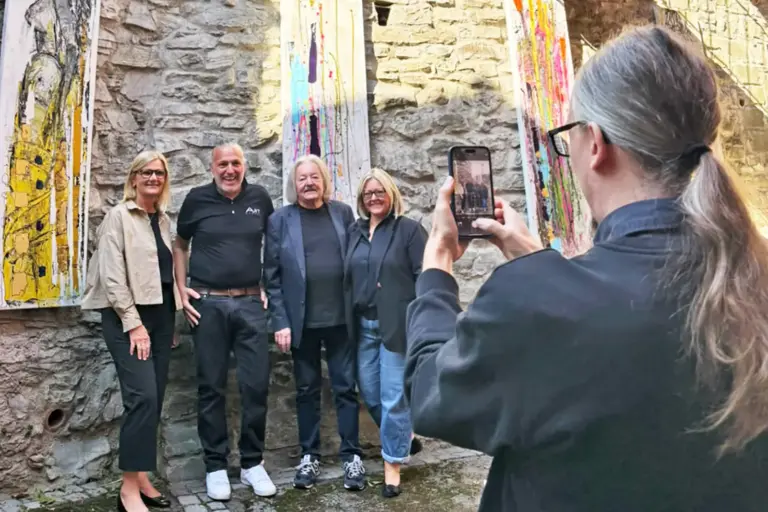 Architektur trifft in Bruck auf Kunst Zwei Frauen und zwei Männer werden vor einer Mauer mit Kunstwerken fotografiert