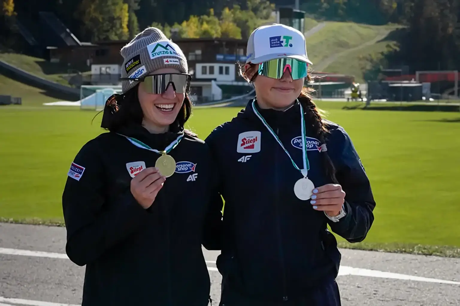 Zwei Sportlerinnen präsentieren im Freien ihre Gold- und Bronzemedaillen.