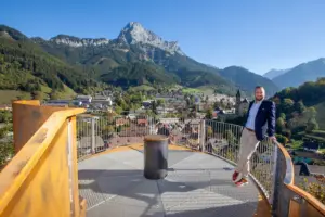 Eisenerz: Ein Auge auf die Stadt Ein Mann steht lächelnd auf einer Aussichtsplattform, im Hintergrund eine Stadt und eine Berglandschaft