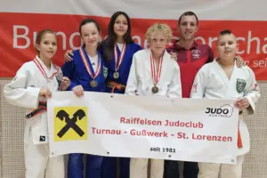Fünf junge Judoka in weißen und blauen Judoanzügen präsentieren ihre Medaillen. Hinter ihnen steht ein Mann in einem roten Poloshirt. Gemeinsam halten sie ein Banner des Judoclubs Turnau–Gußwerk–St. Lorenzen.
