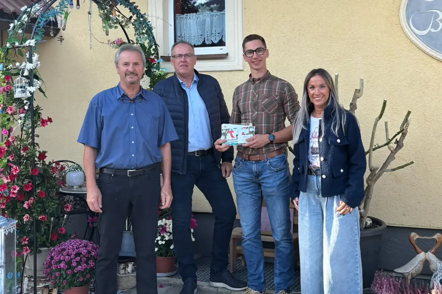 Drei Männer und eine Frau stehen vor einem gelben Haus