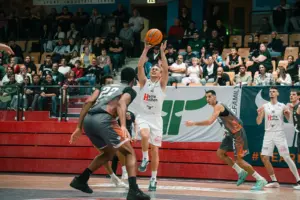Ein Basketballspieler der Kapfenberg Bulls setzt vor mehreren Gegenspielern zum Korbwurf an. Im Hintergrund verfolgen zahlreiche Zuschauer die Partie.