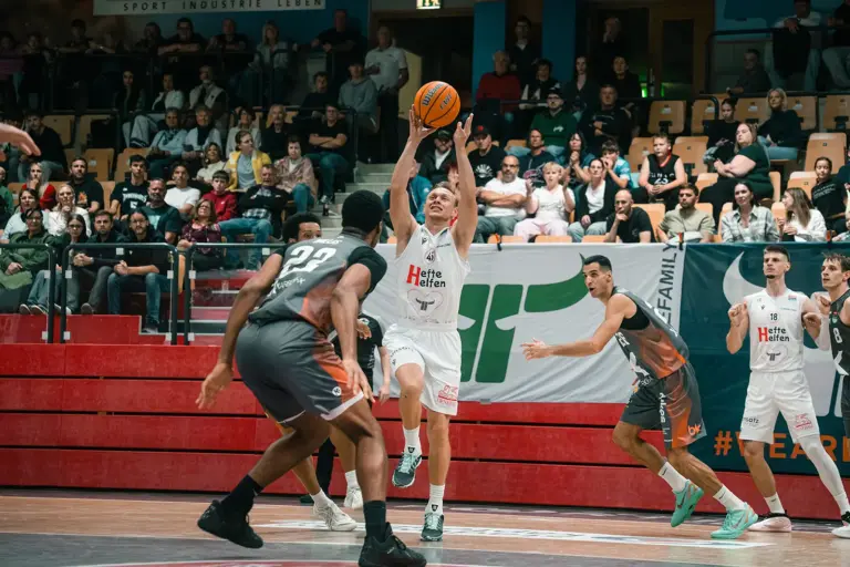 Fünfter Sieg im fünften Spiel für die Kapfenberg Bulls Ein Basketballspieler der Kapfenberg Bulls setzt vor mehreren Gegenspielern zum Korbwurf an. Im Hintergrund verfolgen zahlreiche Zuschauer die Partie.
