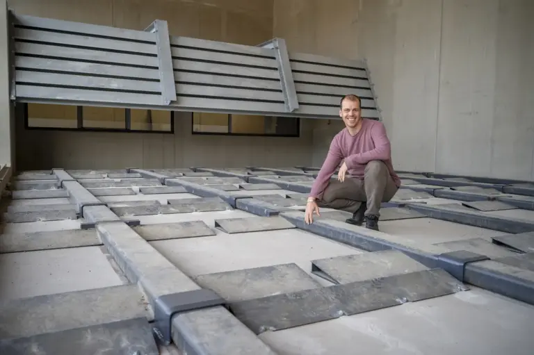Ein Mann kniet auf einer technischen Anlage mit mehreren Metallstreben und Abdeckplatten im neuen Biomasseheizwerk der Stadtwärme Kapfenberg.