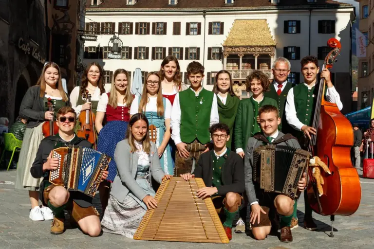 Dreifaches „Sehr gut“ für Kapfenberger Musiker Eine Gruppe Jugendlicher in Tracht steht mit Musikinstrumenten vor einem Haus