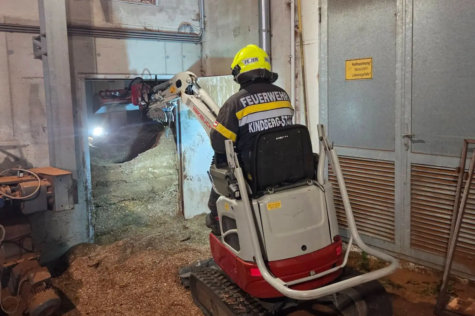 Ein Feuerwehrmann der Feuerwehr Kindberg-Stadt fährt mit einem Minibagger Hackschnitzel aus dem Lagerbereich.