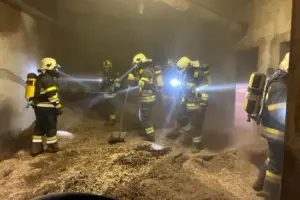 Mehrere Feuerwehrleute mit Atemschutzgeräten suchen und bearbeiten in einem stark verrauchten Hackschnitzellager Glutnester.