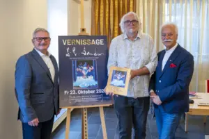 Drei Männer präsentieren ein Plakat zur Vernissage von S. R. Sander in der Galerie K Kindberg.