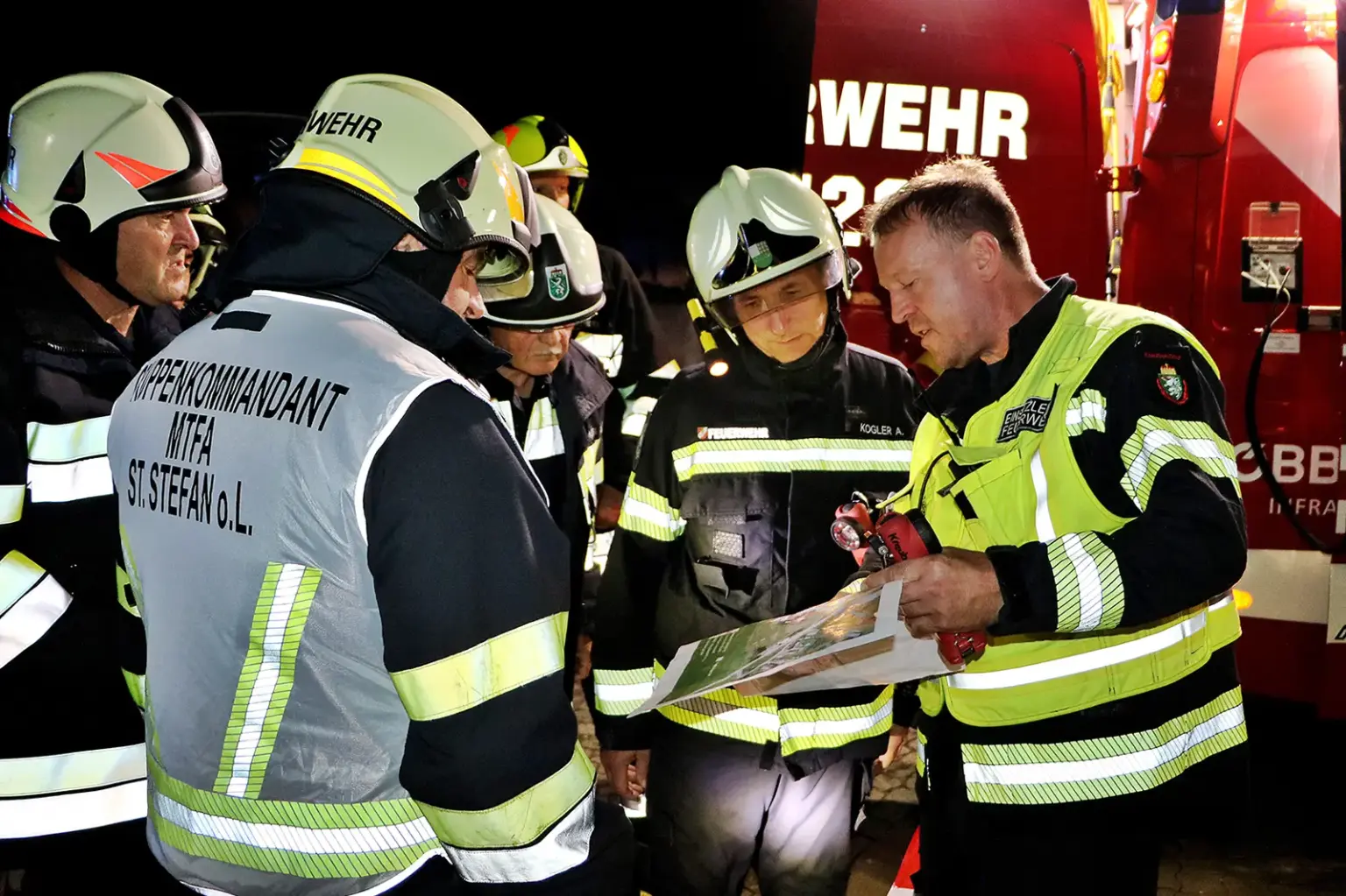 Mehrere Feuerwehrleute beraten sich vor einem Feuerwehrauto