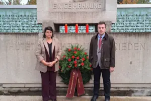 Ein Mann und eine Frau stehen mit einem Kranz vor einem Mahnmal