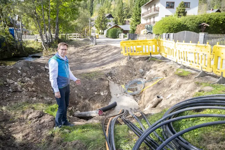 Mariazell: Neues städtisches Wassernetz in Teichmühle Fabian Fluch steht neben einer Baugrube mit freigelegten Leitungen und zeigt auf die Arbeiten beim Wasserleitungsausbau.