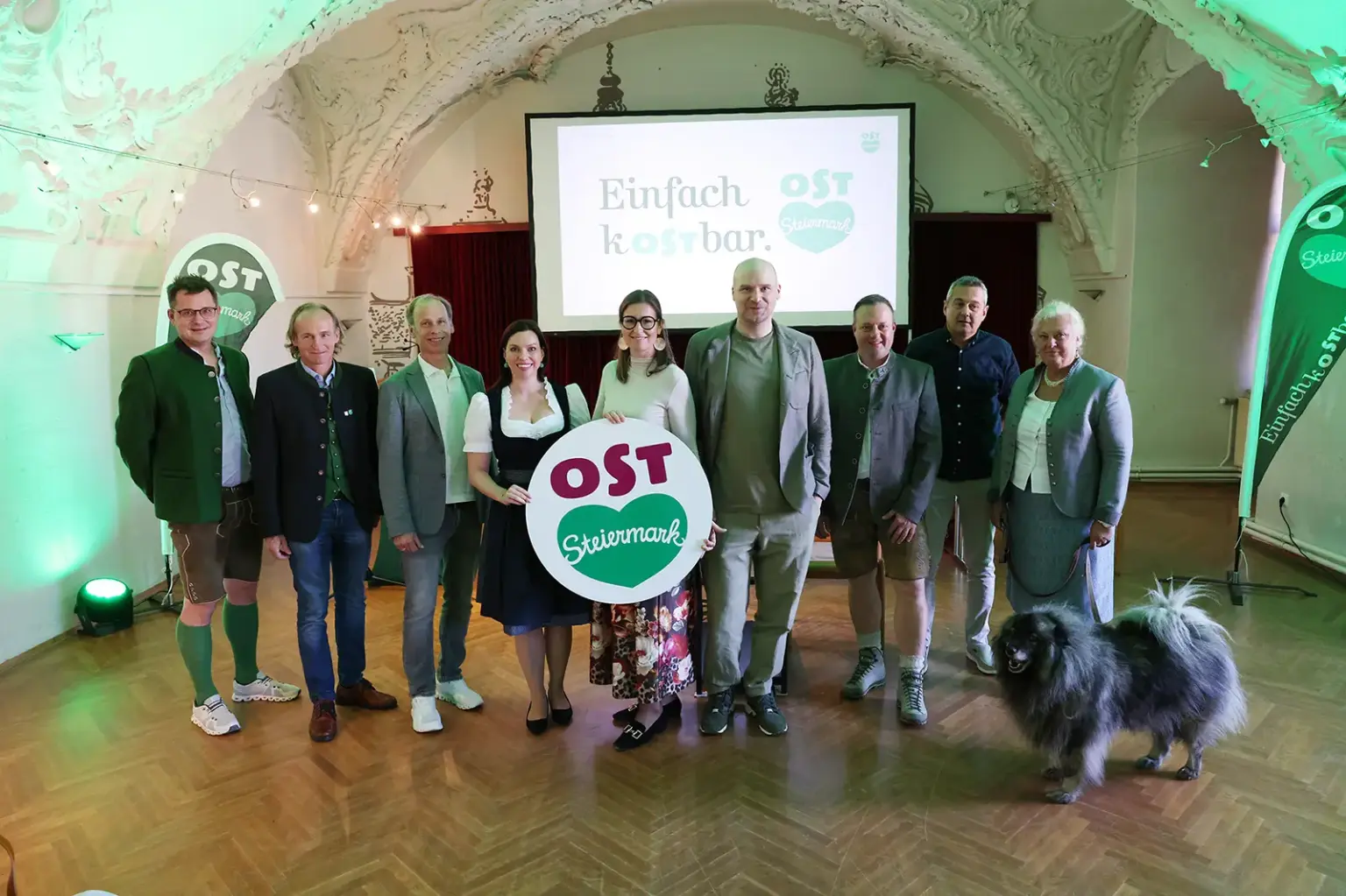 Fachtagung des Tourismusverbands Oststeiermark Ein Gruppe von Personen mit einem Hund steht vor einem Bildschirm in einem großen Saal