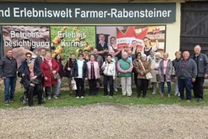Eine Gruppe von älteren Personen steht vor einer mit Fotos beklebten Wand