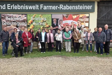 Tagesausflug der Proleber Pensionisten Eine Gruppe von älteren Personen steht vor einer mit Fotos beklebten Wand