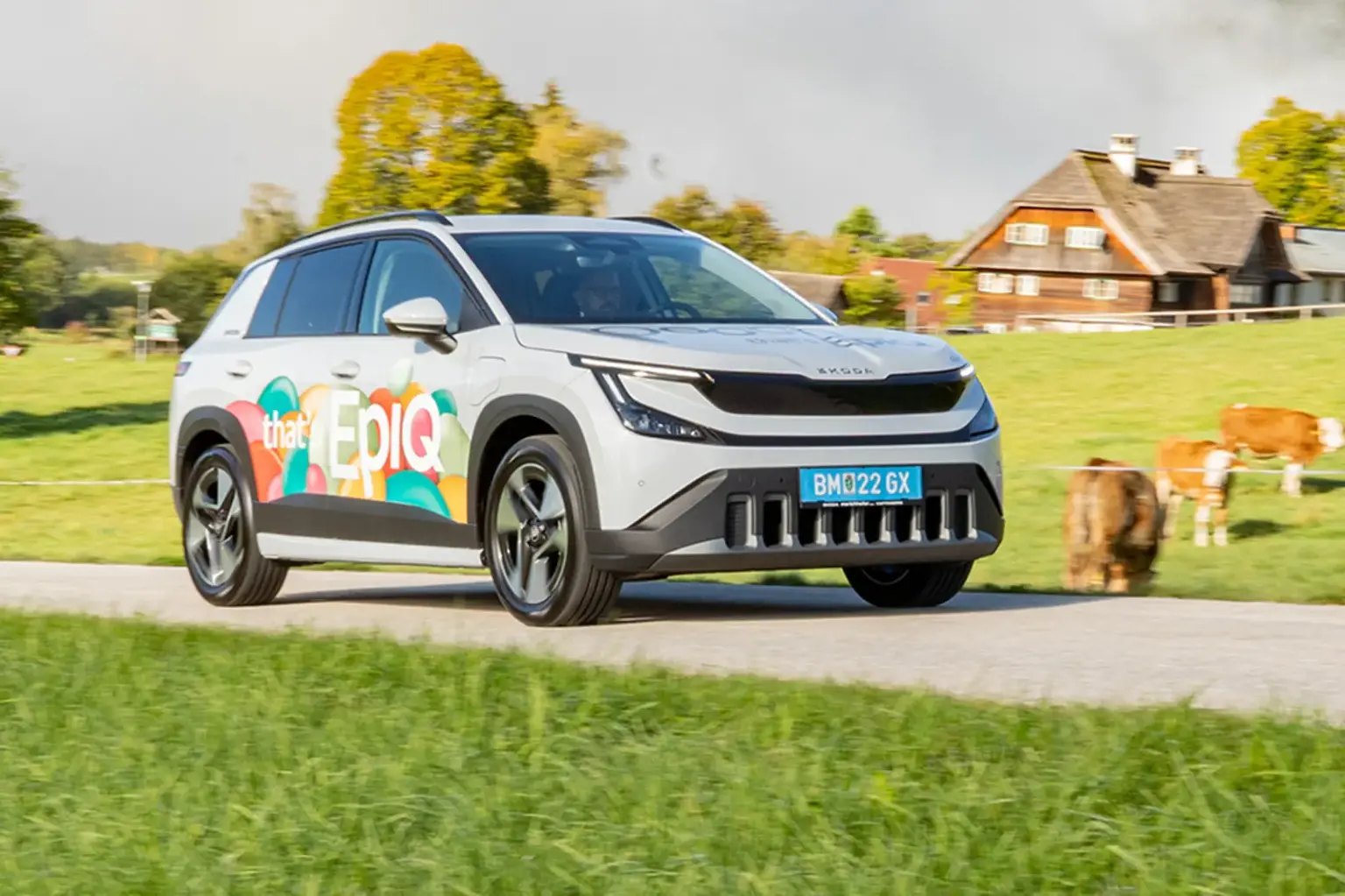 Faktisch praktisch Ein hellgraues Auto der Kategorie Kompakt-SUV mit bunt beklebten Türen fährt auf einer Landstraße von links nach rechts