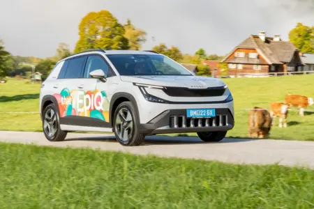 Faktisch praktisch Ein hellgraues Auto der Kategorie Kompakt-SUV mit bunt beklebten Türen fährt auf einer Landstraße von links nach rechts