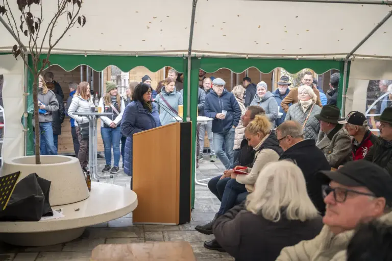 Eine Frau in blauer Jacke spricht an einem Rednerpult unter einem Festzelt. Zahlreiche Besucher verfolgen die Ansprache im Sitzen und Stehen.