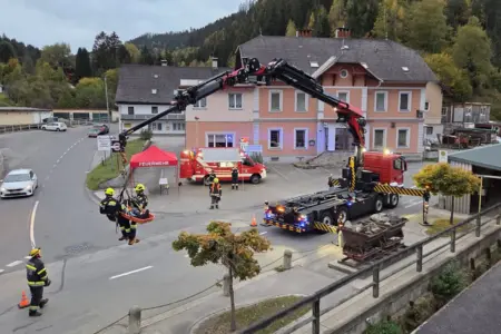 Ein Kranwagen mit Feuerwehrleuten vor einem roten Haus