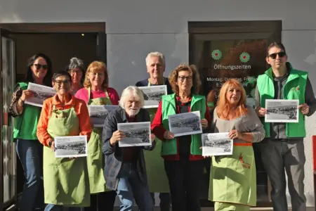 Kalender zeigt St. Barbara damals und heute Neun Personen präsentieren vor einem Haus Kalender