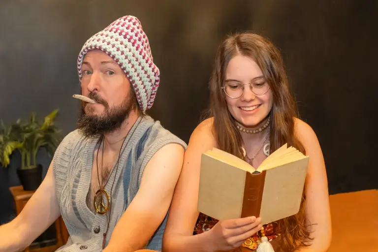 Ein rauchender Mann und eine lesende Frau sitzen an einem Tisch