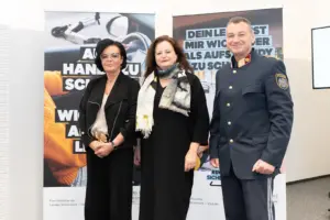Ein Mann in Uniform und zwei Frauen stehen vor zwei Roll-ups