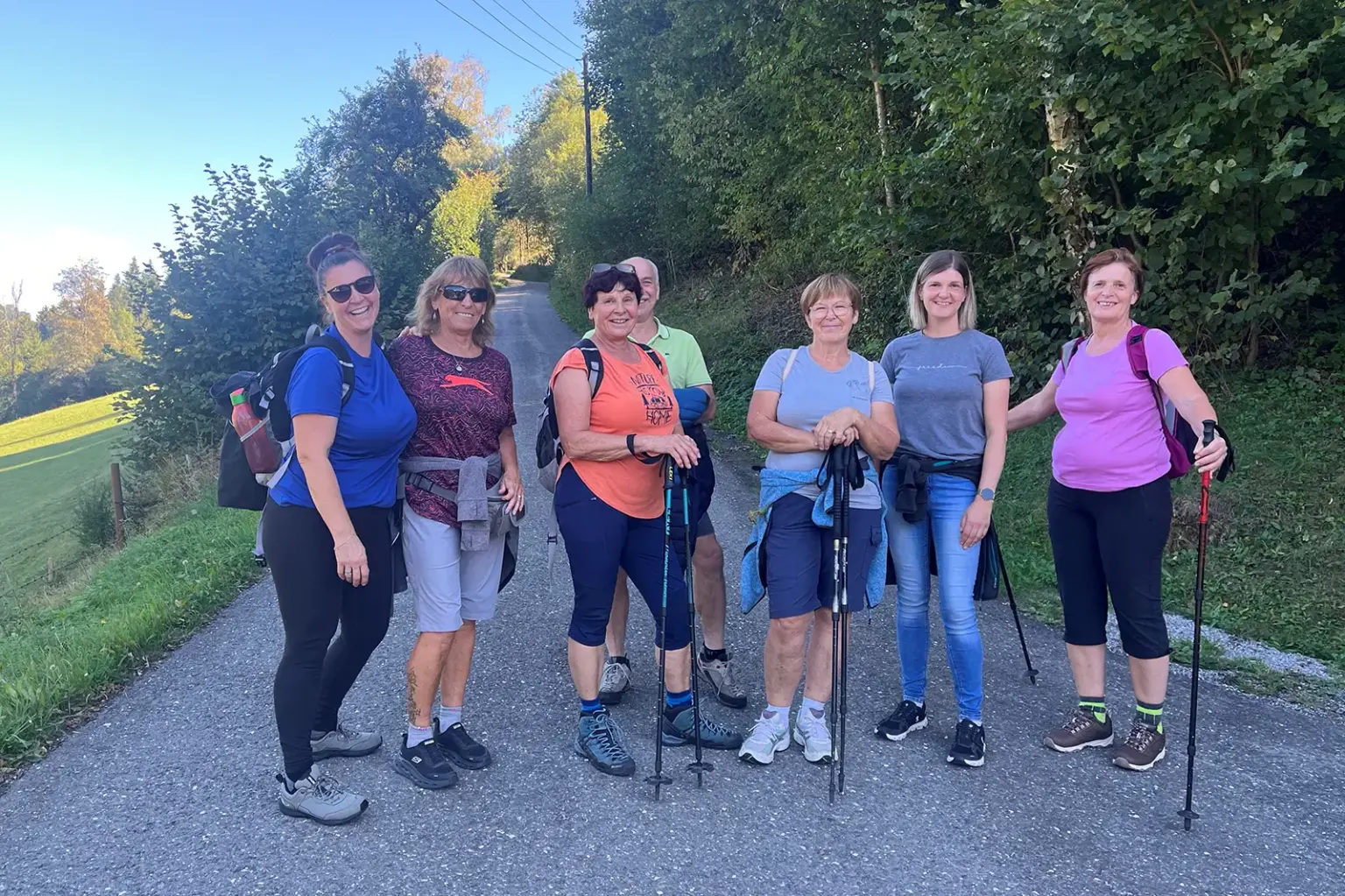 Eine Wandergruppe mit sieben Personen macht bei sonnigem Wetter auf einem von Bäumen gesäumten Weg in Tragöß-St. Katharein Halt. Einige Teilnehmer tragen Rucksäcke und Wanderstöcke.