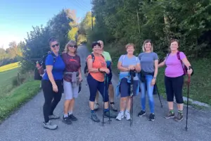 Eine Wandergruppe mit sieben Personen macht bei sonnigem Wetter auf einem von Bäumen gesäumten Weg in Tragöß-St. Katharein Halt. Einige Teilnehmer tragen Rucksäcke und Wanderstöcke.