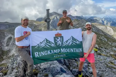 Turnau: Ein Berg, der ihren Namen trägt Drei Männer stehen lächelnd bei einem Gipfelkreuz und halten eine Flagge