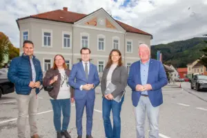 Zwei Frauen und drei Männer stehen lächelnd auf einem innerörtlichen Platz vor einer sanierten Gebäudefassade