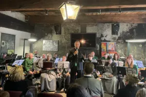 Ein Mann im Bergmannskittel spricht vor sitzenden Musikern in ein Mikrofon