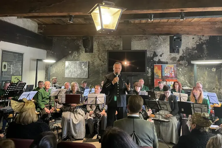 Vordernberg: Abschied vom „Mythos Erz“ Ein Mann im Bergmannskittel spricht vor sitzenden Musikern in ein Mikrofon